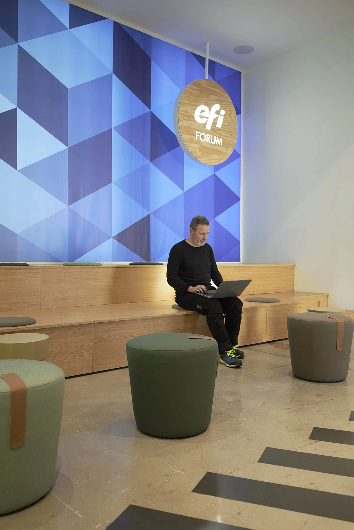Pufs tapizados y banco de madera en el foro de las oficinas EFI en Almassora