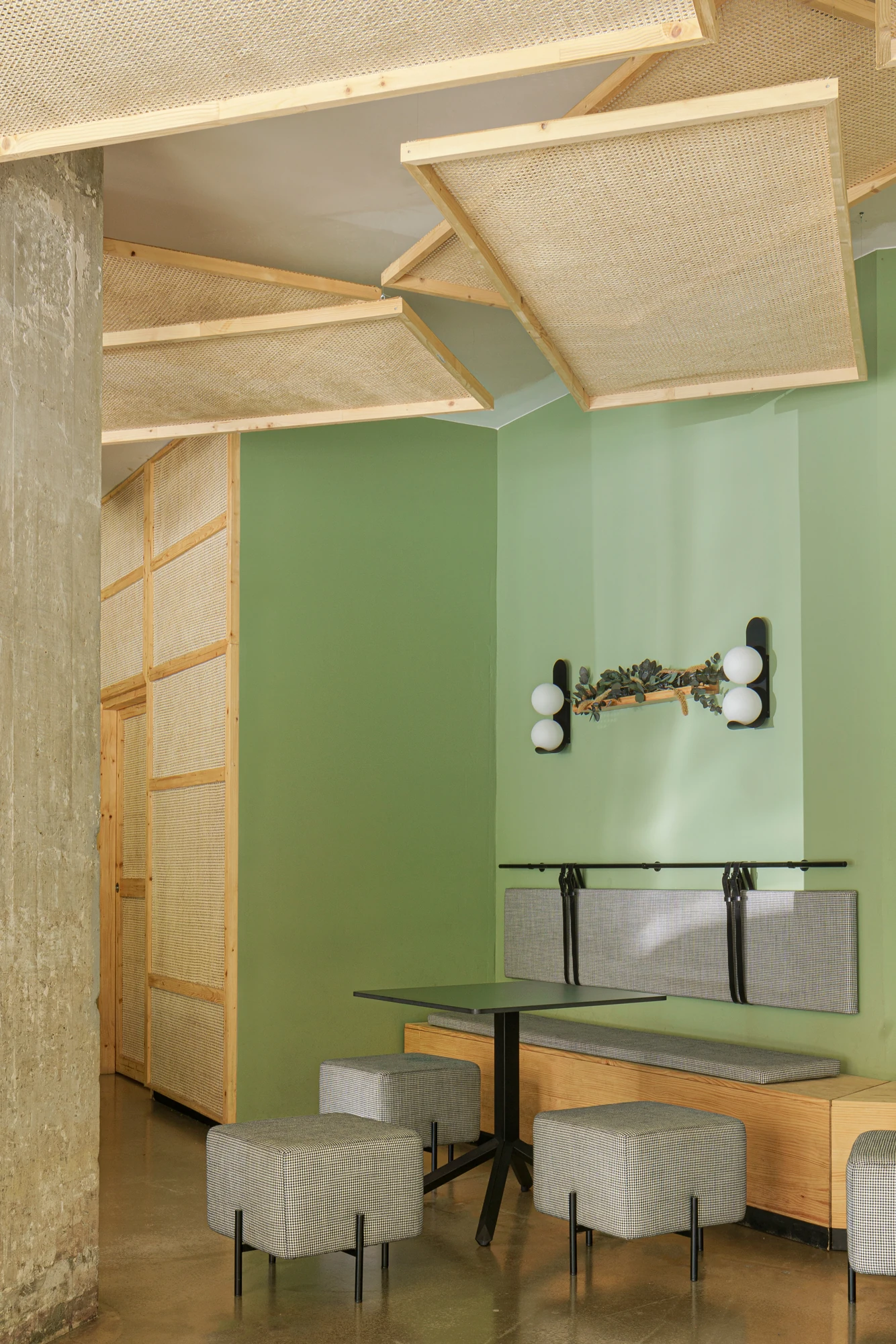 Mesa y asientos junto a la pared verde de Nougat, en el proyecto de Viruta Lab